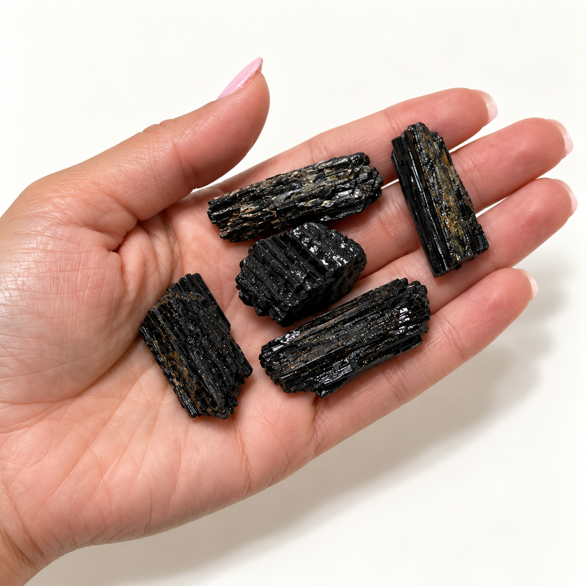 Natural raw black tourmaline crystals displayed in a hand to show approximate size